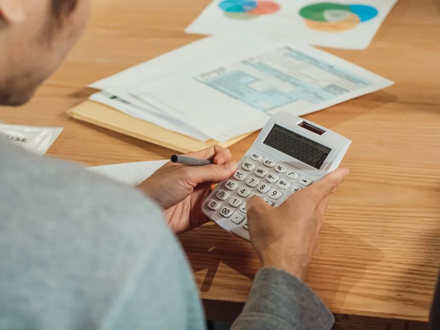 Hands working a calculator beside financial documents — AI consulting rates and project fees explained for buyers in 2026